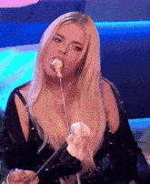 a woman with long blonde hair is eating a piece of food on a stick