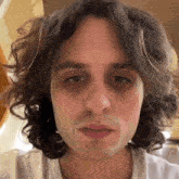 a close up of a man 's face with curly hair and a white shirt .