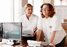 two women standing next to each other in front of a computer monitor .