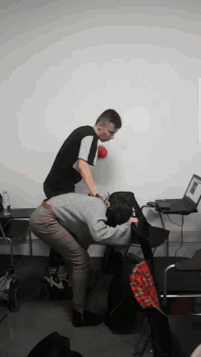 a man and a woman squatting down with a laptop on a desk