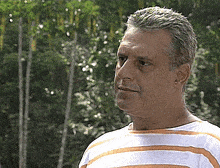 a man wearing a white and orange striped shirt is standing in front of trees