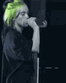 billie eilish is drinking water from a bottle while standing on stage .