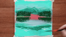 a person is painting a lake with mountains in the background .