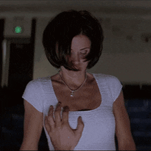 a woman in a white shirt has her hand on her chest