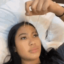 a woman is laying in bed holding a necklace in her hand and looking at it .