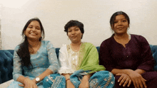 three women sit on a blue couch smiling for the camera