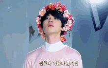 a man with a flower crown on his head is wearing a pink sweater and looking up