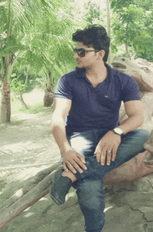 a man in a blue shirt sits on a tree branch with his legs crossed