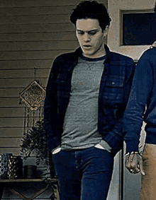 a man in a plaid jacket and a gray shirt is standing in front of a door .