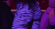 a woman in purple zebra print pants is standing in front of a purple background .