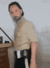 a man in a walking dead costume is standing in front of a white wall holding a sword .
