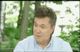 a man in a blue shirt is sitting on a bench in a park and making a funny face .
