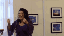 a woman in a purple dress is standing in front of a wall with paintings on it