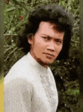 a man with curly hair and a beard is wearing a white shirt .