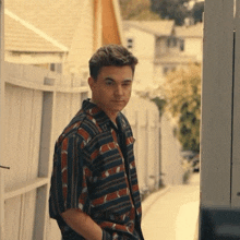 a young man in a striped shirt stands in front of a fence