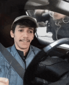 a man wearing a hat is driving a car and the steering wheel says sh