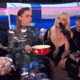 a group of people are sitting around a table with a woman holding a red bowl with a cross on it .