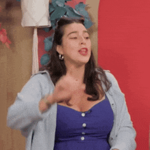 a woman in a blue dress and a light blue cardigan is making a funny face