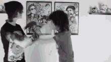 a couple of people are standing next to each other in front of a wall with paintings on it .