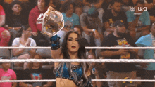 a woman in a wrestling ring is holding a championship belt in front of a crowd
