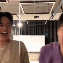 two men are laughing in a room with a whiteboard in the background .