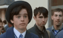 a group of young men are standing next to each other and one of them is wearing a hat and tie .