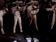 a man in a mariachi outfit is dancing on a stage with a band .