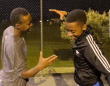 two young men are standing next to each other in front of a chain link fence .