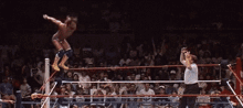 a wrestler is jumping in the air while a referee looks on