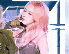 a woman with pink hair is standing next to a man in a green jacket on a stage .