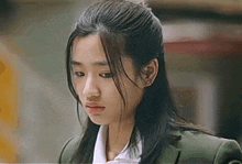 a close up of a young woman with long hair wearing a green jacket and white shirt .