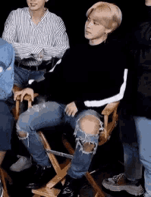 a man in ripped jeans is sitting in a director 's chair with his legs crossed .