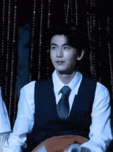 a young man wearing a vest and tie is sitting in front of a curtain .