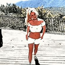 a woman in a white top and shorts is standing on a wooden deck