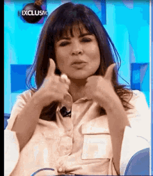 a woman is giving a thumbs up sign while sitting in front of a blue background .