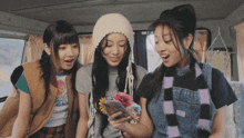 three girls are looking at a cell phone and one has a flower in her hand