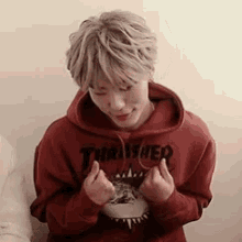 a young man wearing a red thrasher hoodie is sitting on a couch .