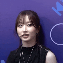 a woman wearing a black top and a microphone stands in front of a blue wall .
