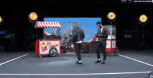 two men are dancing in front of a ice cream cart