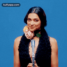 a woman is holding a microphone and a flower in her mouth .