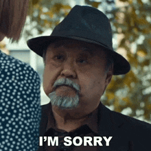 a man with a hat and a beard is saying i 'm sorry to a woman .