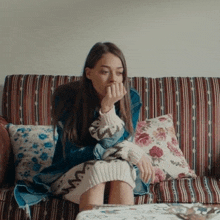 a woman is sitting on a striped couch with a floral pillow