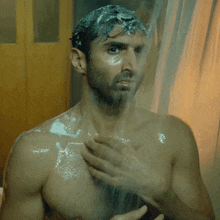 a shirtless man is taking a shower with foam on his head