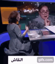 a woman wearing glasses is sitting at a desk in front of a microphone with a sign that says gifs.com