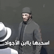 a man in a hat is standing next to another man with arabic writing on the bottom
