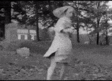 a black and white photo of a woman in a white dress walking in a cemetery .