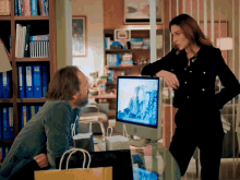 a man and a woman are standing in front of a computer with a mountain on it