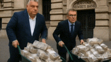 two men are pushing a wheelbarrow full of money in front of a building that says ' nemzeti bank ' on it