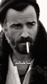 a man with a beard is smoking a cigarette in a black and white photo with arabic writing on it .