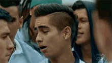 a man with a mohawk is standing in a crowd of people and making a funny face .